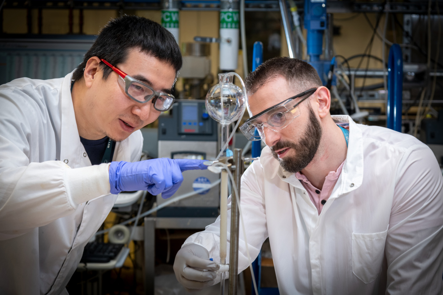 Two men looking at something made of glass in the lab together, both wearing PPE