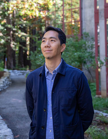 Daniel Kim, a young Asian man in casual professional clothes, standing in the redwoods