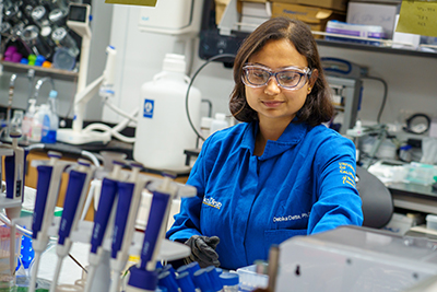 A woman with a brown bob working in a lab, wearing PPE