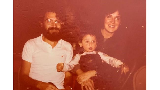 Sepia-toned photograph of a bearded man seated next to a brunette woman holding a young child wearing overalls