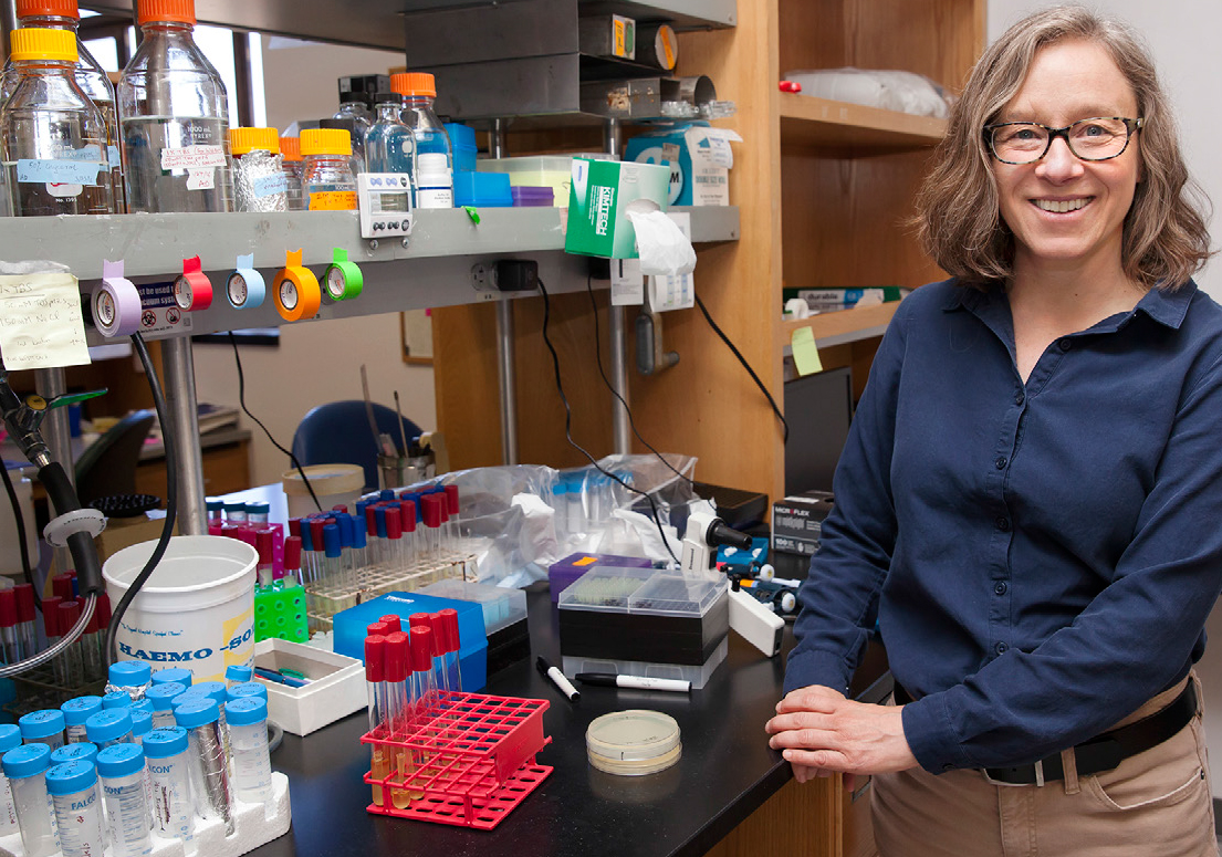 Kathy Collins smiles at the camera next to a lab bench with test tubes and equipment