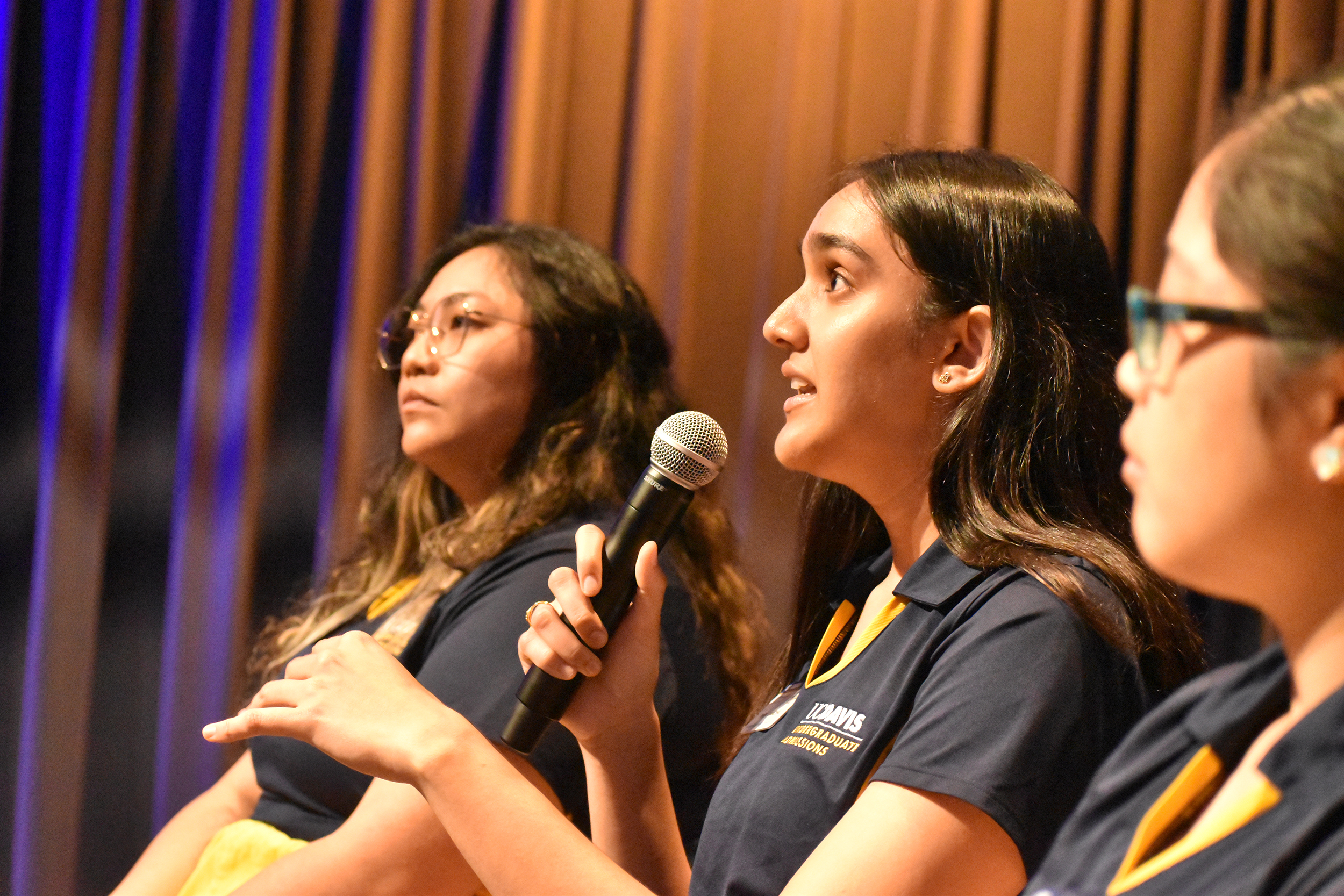 A woman with long dark hair talks into a microphone