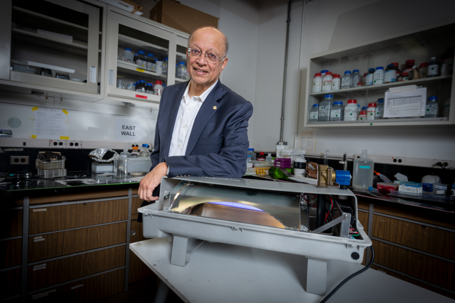 Ashok Gadgil, wearing a suit, leans on a piece of lab equipment and smiles for the camera in a laboratory