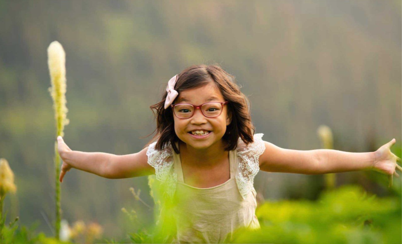 Ada Finlayson in a field of wildflowers, smiling at the camera with arms wide open.