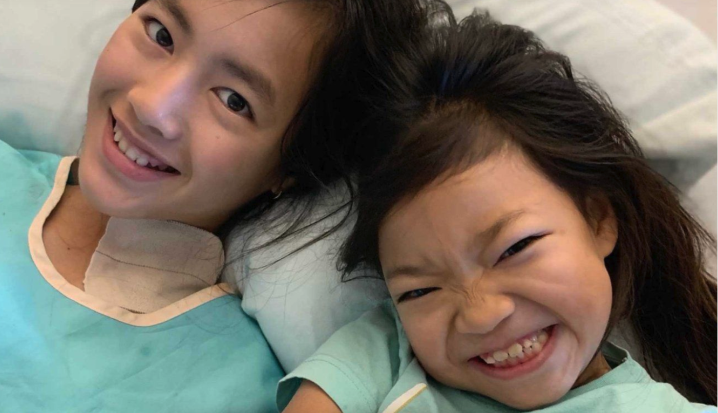 Ada and Lily Finlayson, school-aged, take a selfie wearing green medical gowns.