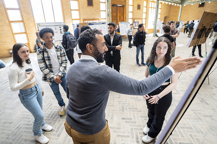 Aaron Streets presents a poster to four onlookers in a well-lit conference hall