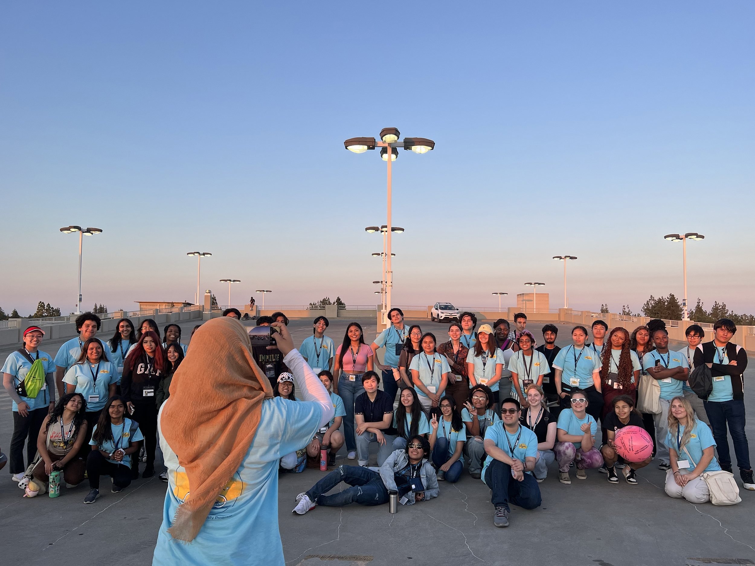 Students pose for a group shot while a person wearing a headscarf takes a picture