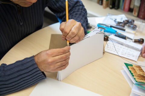 Shot of hands using a pencil to bind several pages of a hand-made book together. 