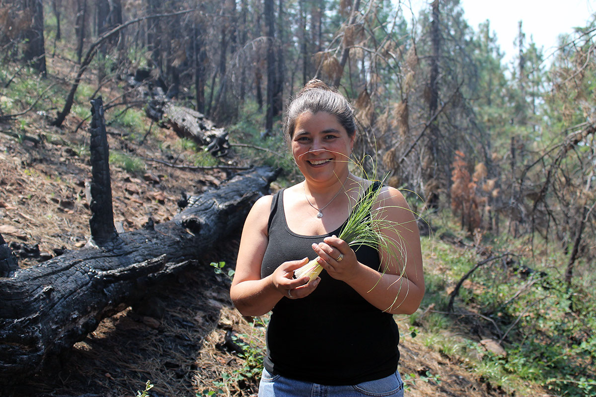 Carolyn Smith holds a bunch of green grass in a recently-burned forest