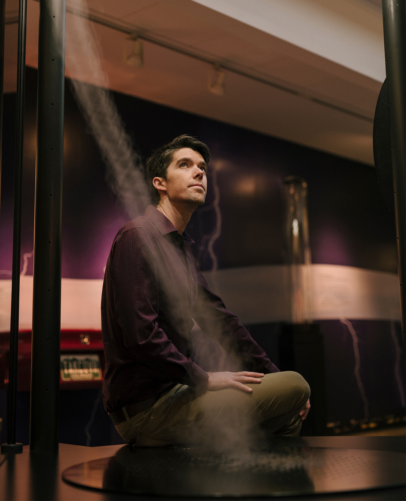 Daniel Swain sits in a darkened room, looking up to the right of the frame, with a trail of steam cutting across his shoulder.