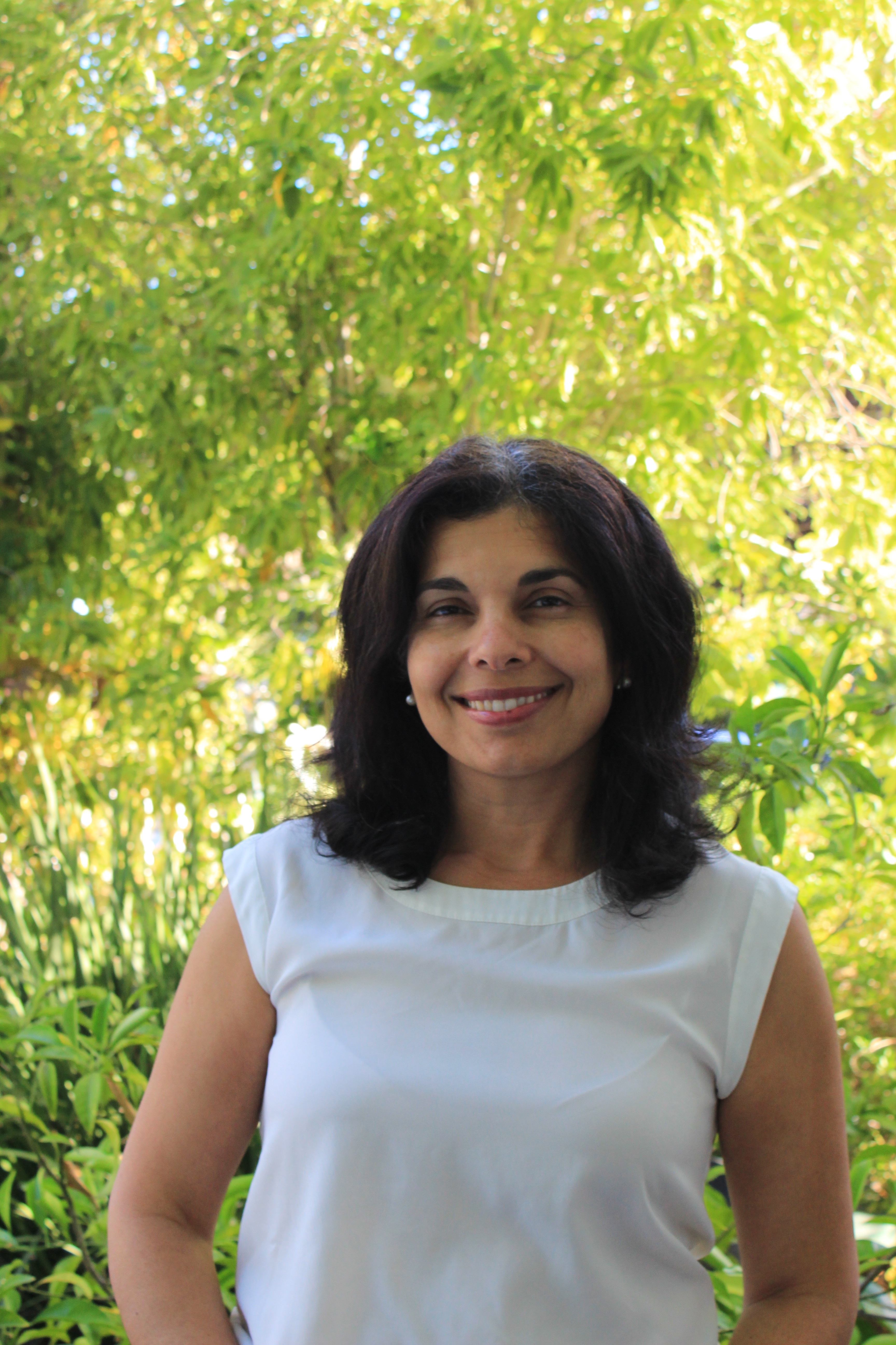 Arianne Teherani smiles from the camera in a hips-up portrait with sun-bleached greenery in the background