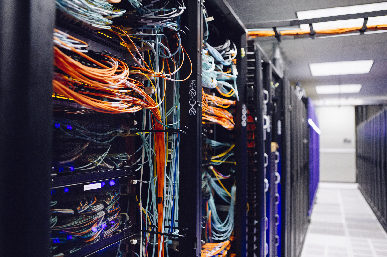 The inside of a supercomputer, showing a nest of brightly colored wires, mostly orange and black.