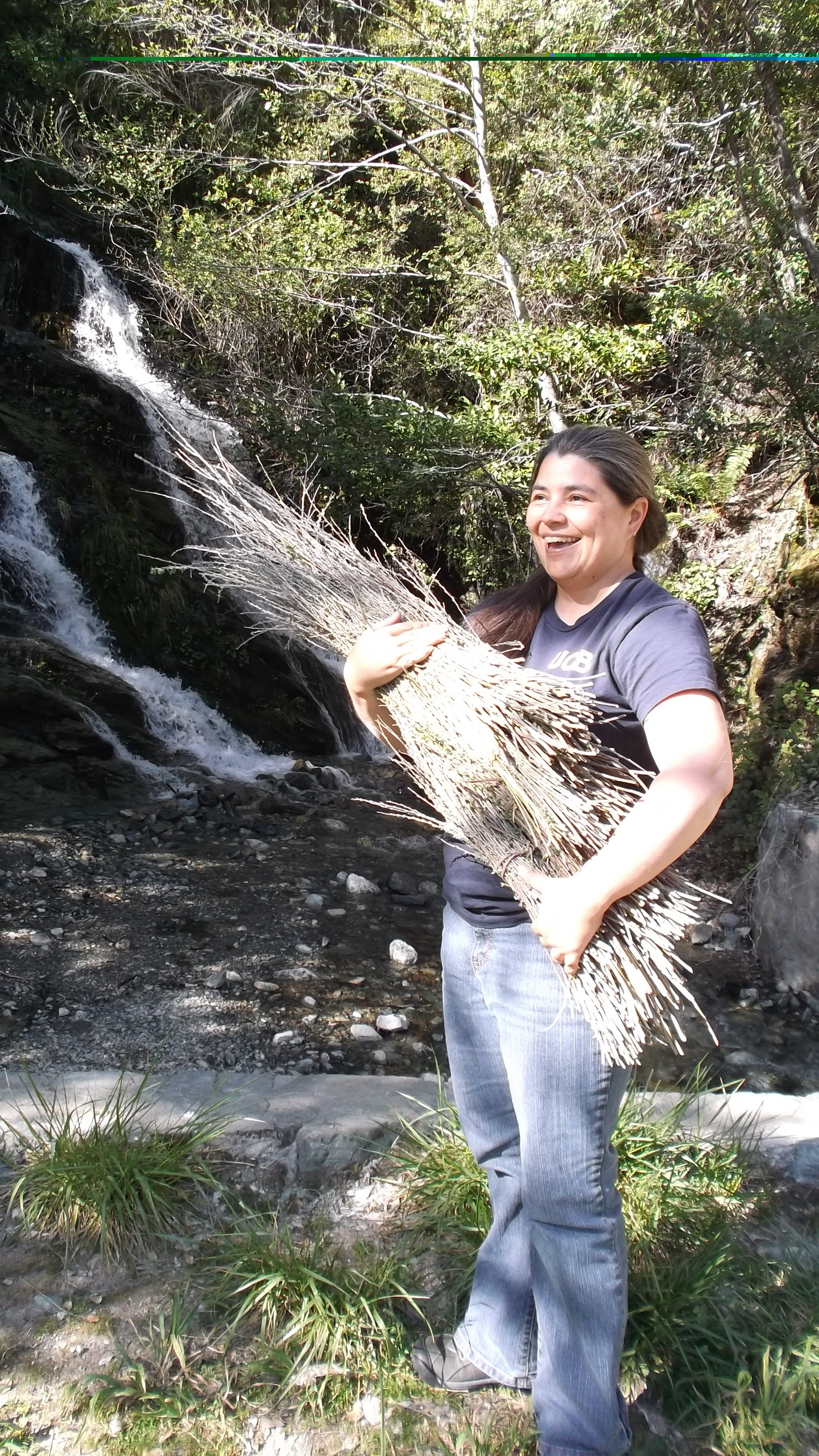 Carolyn Smith holds an armful of dry sticks, standing in front of a waterfall