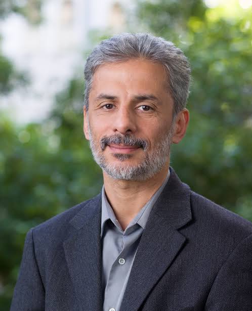 Shoulders-up portrait of Wael Al-Delaimy, who looks frankly at the camera wearing a dark suit jacket and gray button up shirt