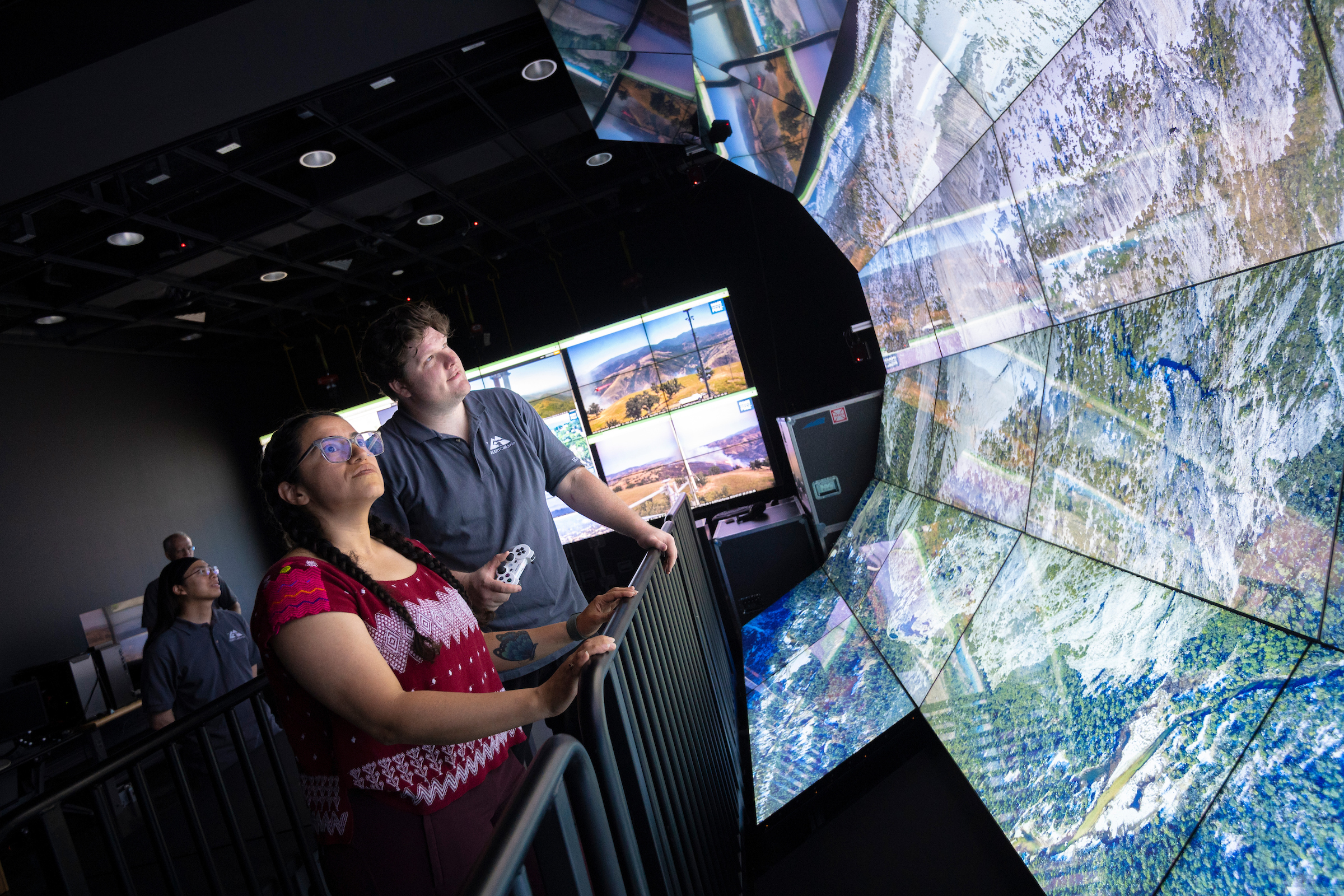 A man and a woman stare at a video screen shaped like a wave with topographical info on it