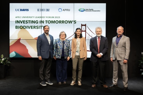 Five people in business attire stand in front of a video screen reading "Investing in Tomorrow's Biodiversity"
