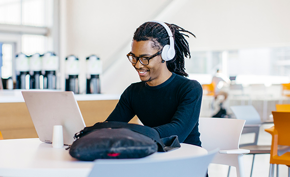 Young African American man smiling with headphones on working on a computer