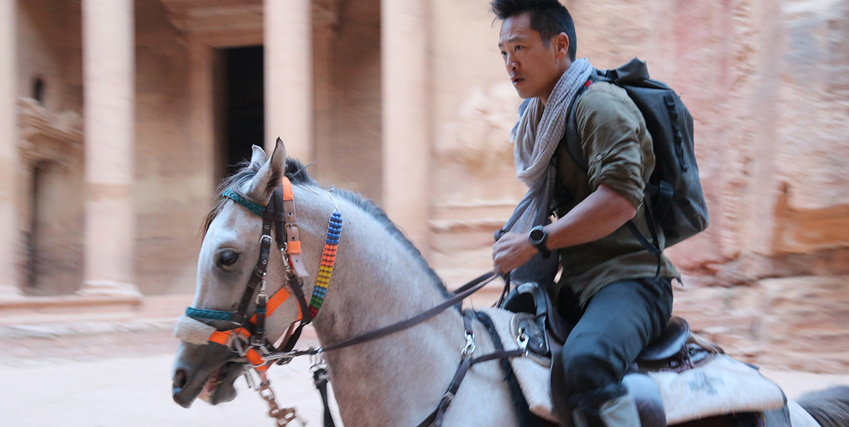 Albert Lin riding on a horse past an ancient temple