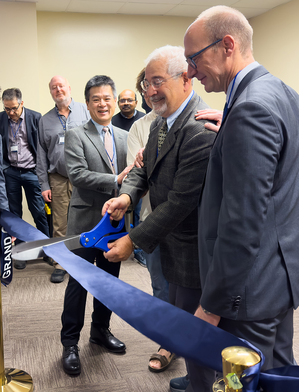 Small group of men in formal clothes cutting a ribbon indoors