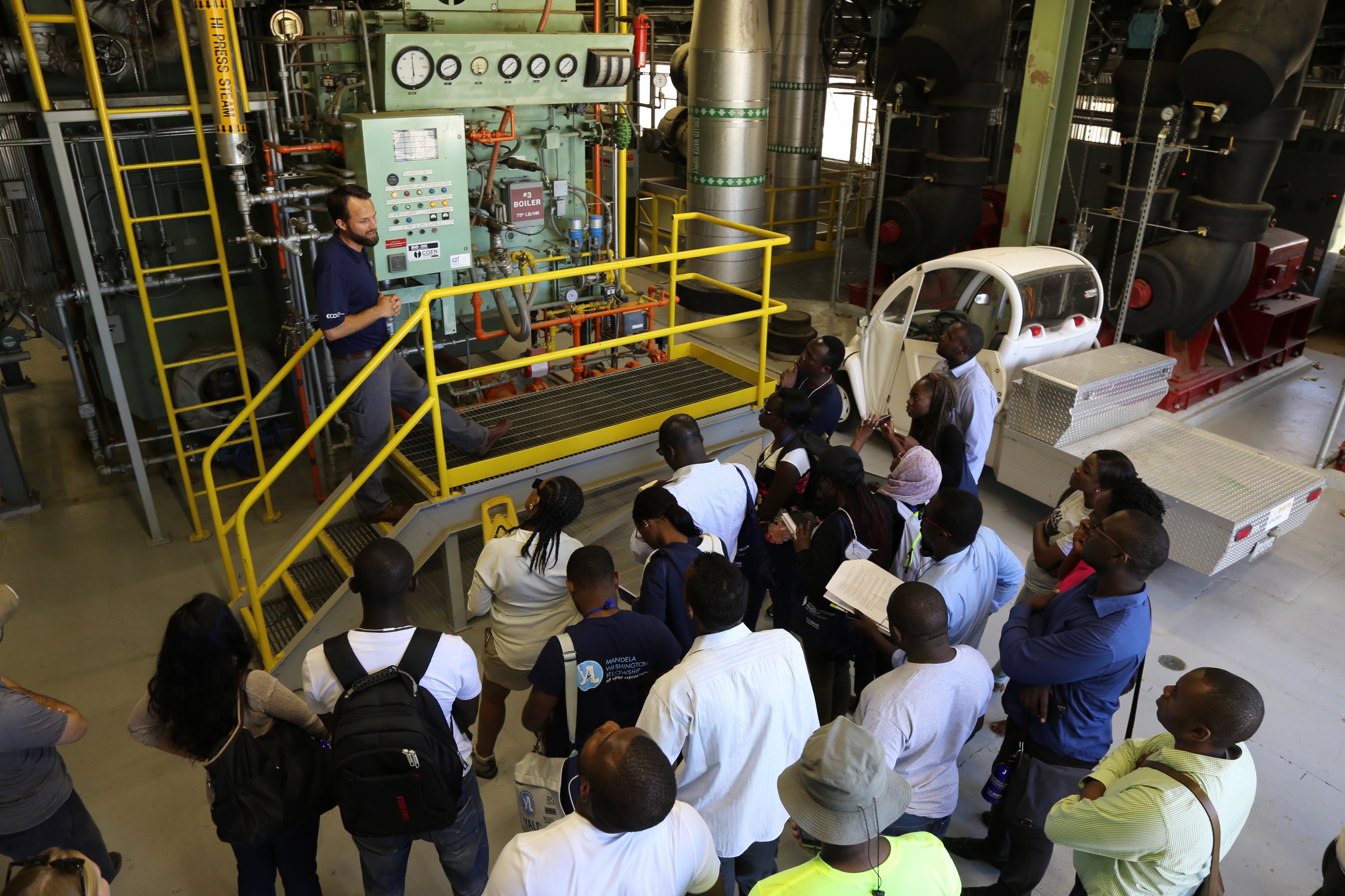 Josh Morejohn stands in front of an old steam boiler, speaking to a group of visitors on a tour.