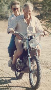 An old photo of a man and a woman on a motorbike on sand
