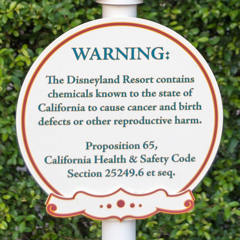 A circular sign reading "WARNING: The Disneyland Resort contains chemicals known to the state of California to cause cancer and birth defects or other reproductive harm. Proposition 65, California Health & Safety Cod Section 2549.6 et seq."