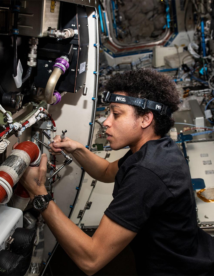 Jessica Watkins wears a headlamp and works with complicated looking machinery inside the International Space Station