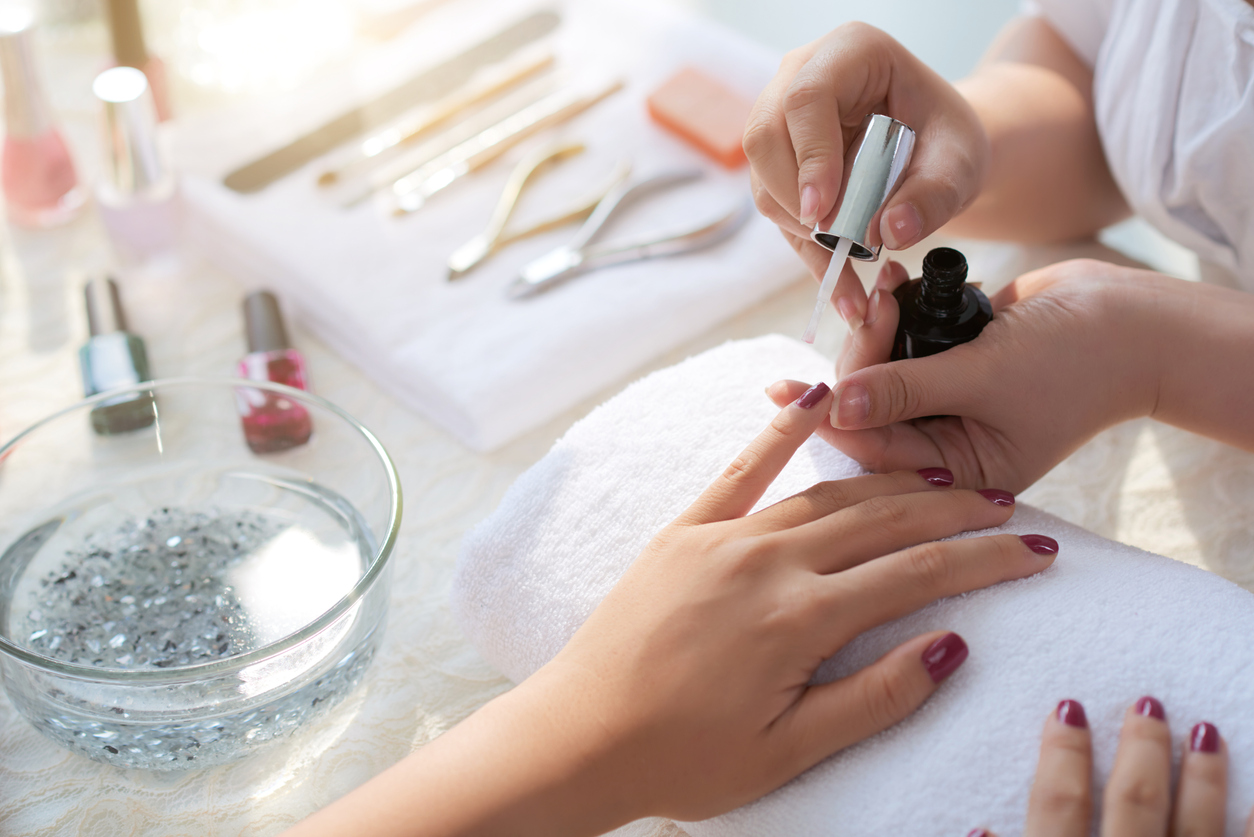 A manicurist paints a customer's fingernails dark red.