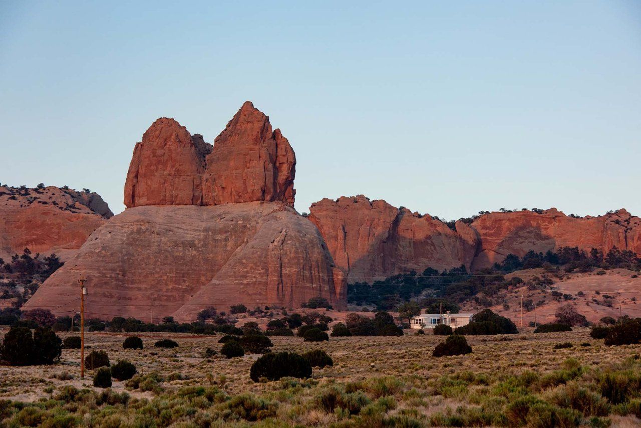 Red sandstone cliffs/bluffs at sunset under a clear sky, with a mobile home parked at the base