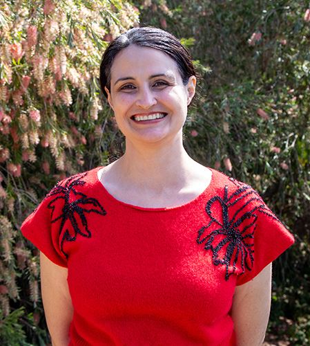 Samantha Gorman, brunette, smiles for camera in red shirt with black embroidery at shoulders