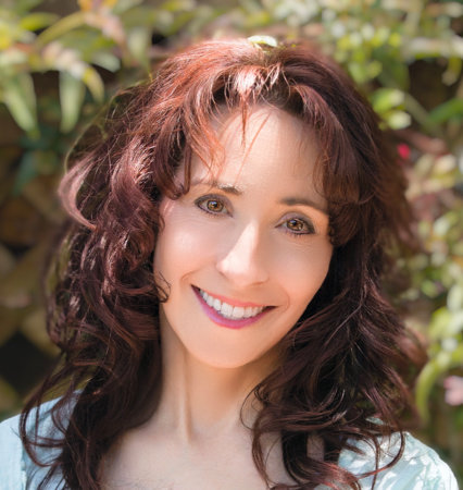 Elissa Epel smiles for a shoulders-up portrait outside with greenery in the background