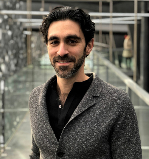 Ziad Obermeyer, bearded with dark hair, smiles at camera in chest-up portrait, with a modern architecture in the background