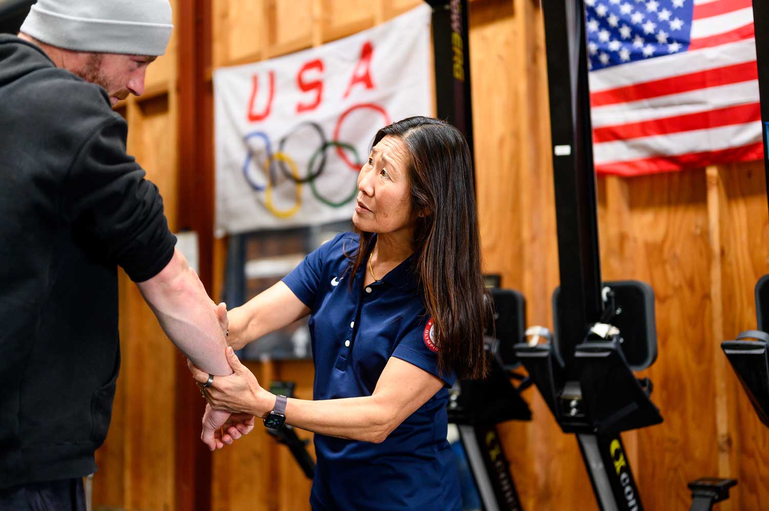 Ben Davison, left, receives physical therapy on his arm from Dr. Cindy Chang, right. On a wall in the background are an American flag and a Team USA Olympic flag.