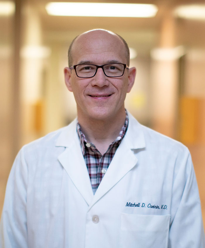 Bald smiling man with glasses wearing a lab coat