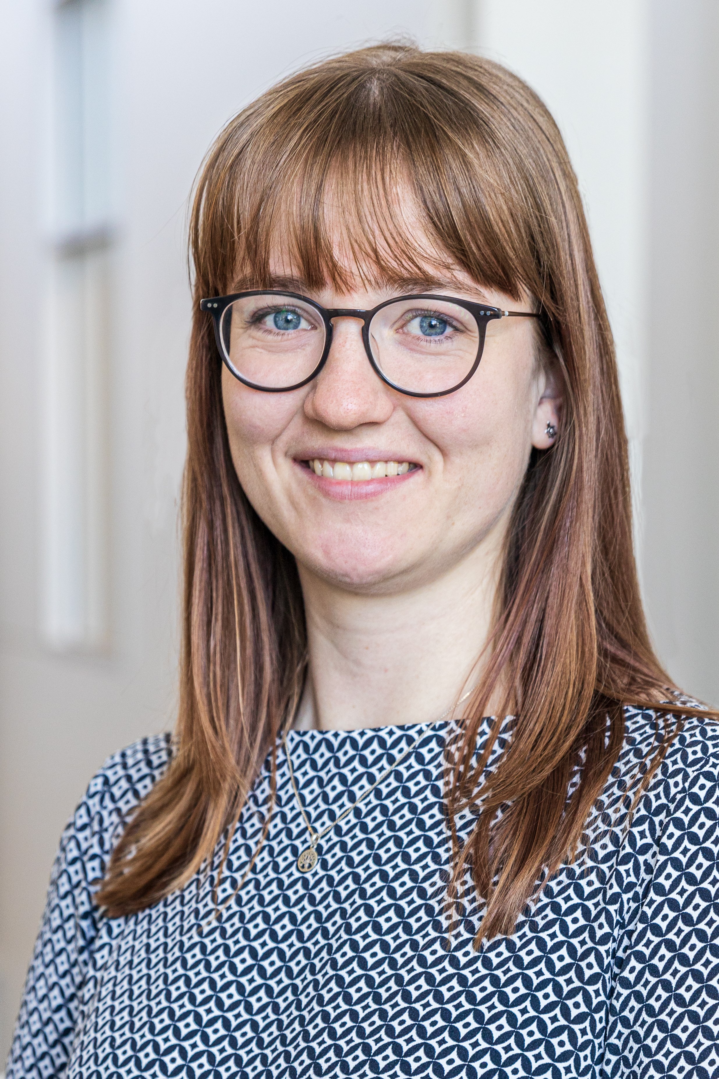 Marie Buhl, wearing a blue and white blouse and horn-rimmed glasses, with straight red hair, smiles for a professional portrait