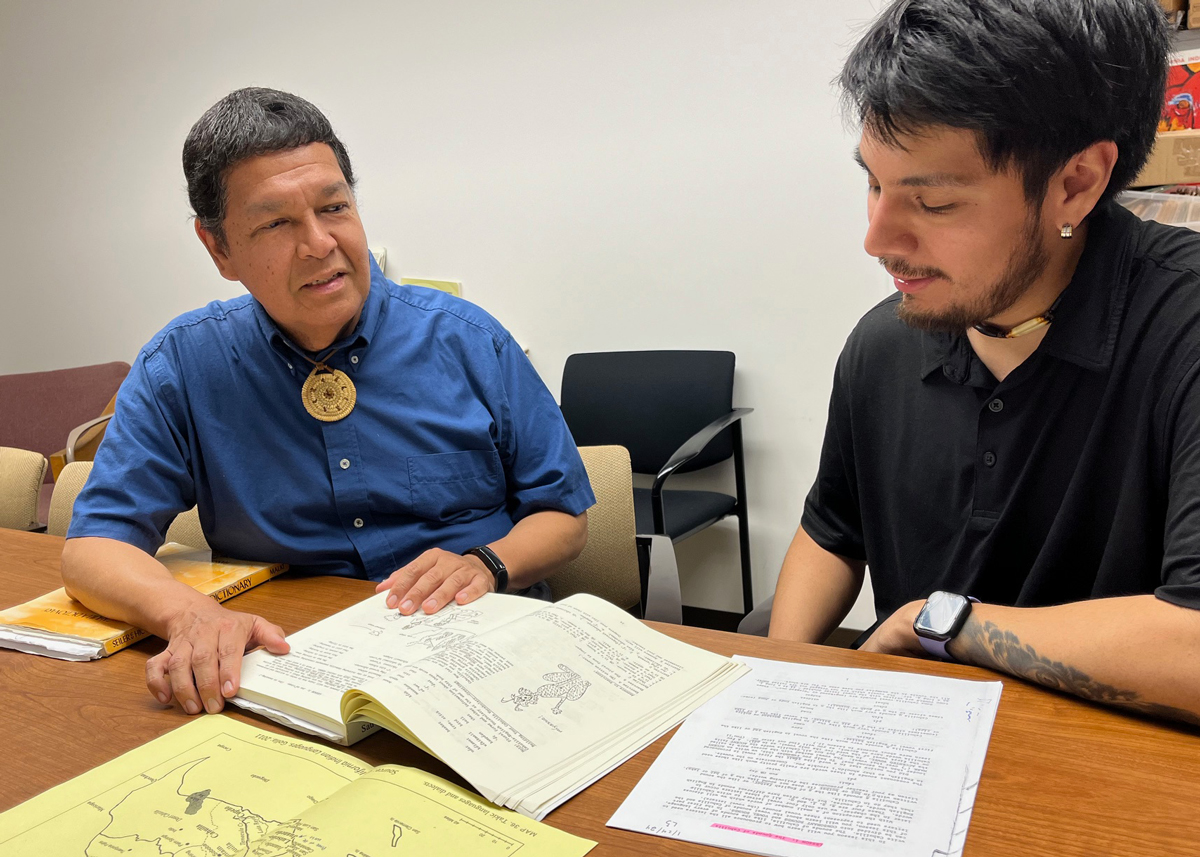 Two people sitting at a table together looking at class materials