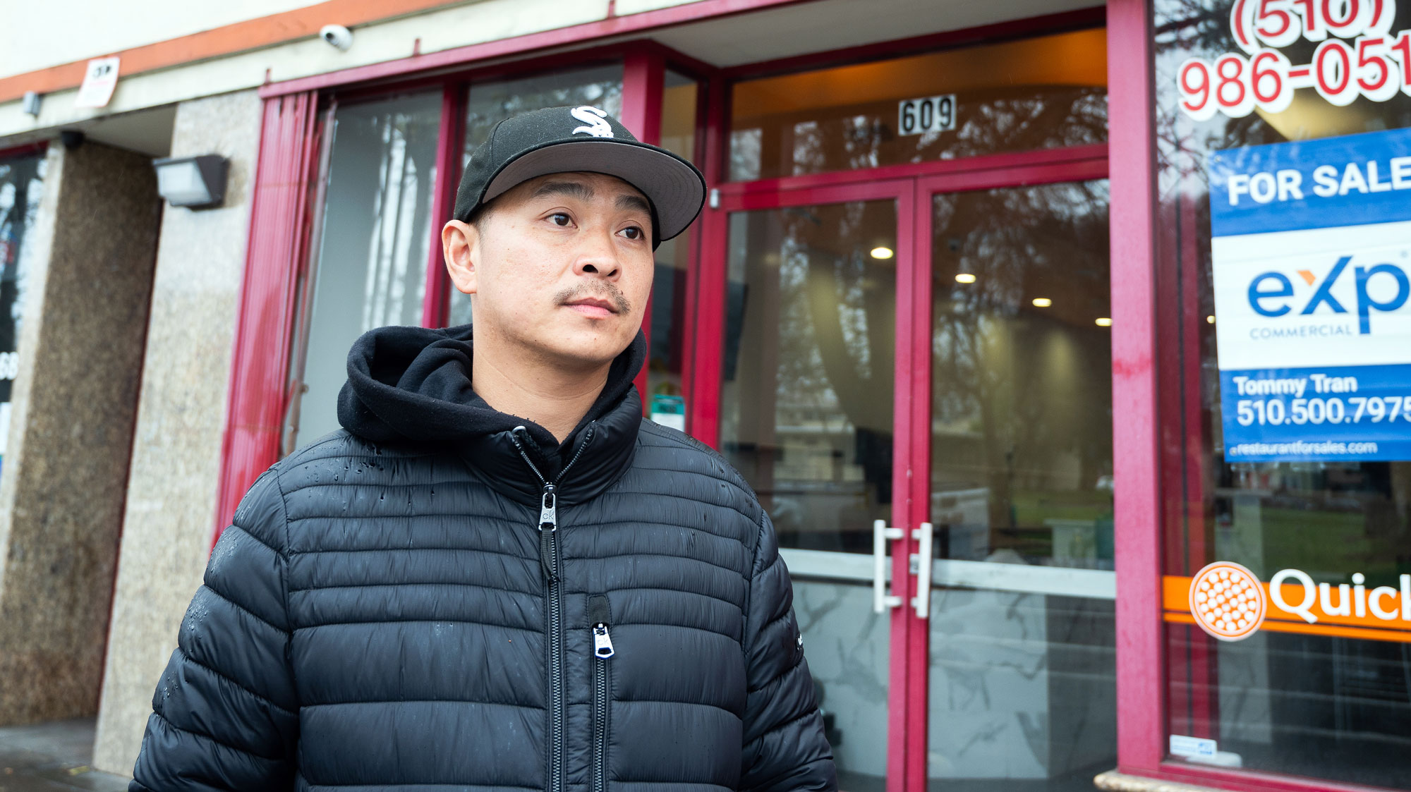 Chien Nguyen outside his restaurant with a somber expression, looking away from the camera
