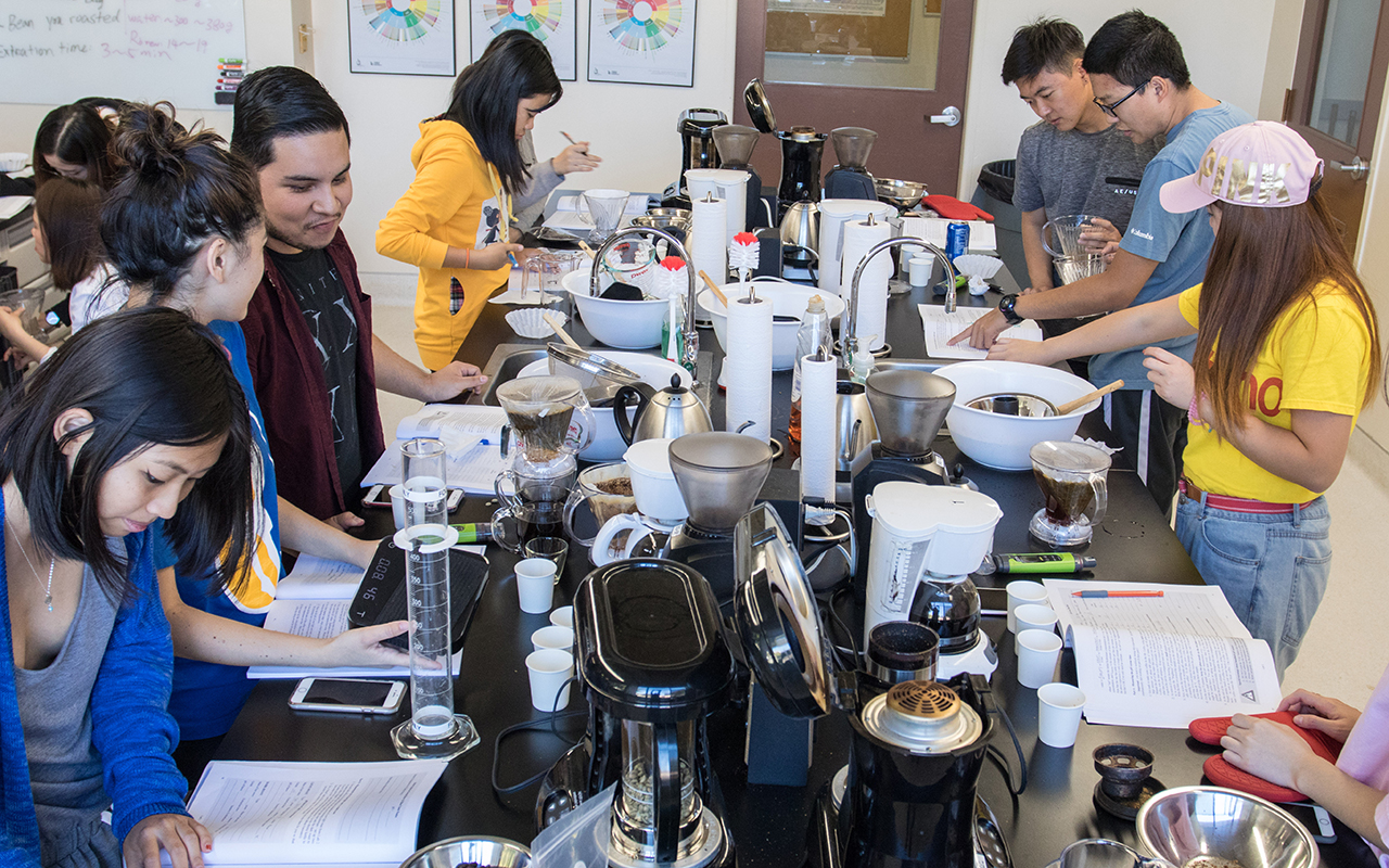 students working around a table covered with coffee-making apparatus