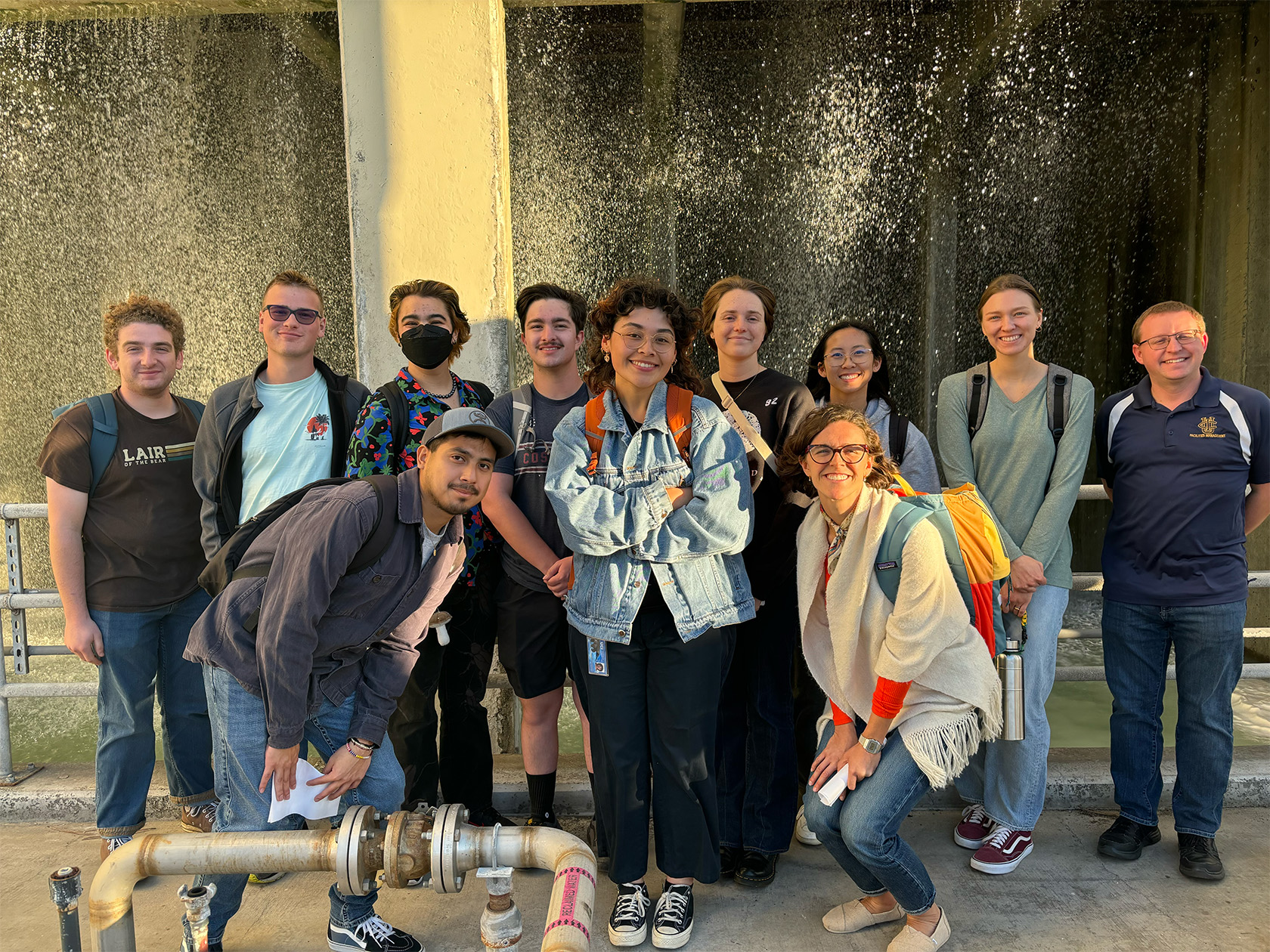 12 people pose for a picture in an industrial-looking facility. Jazmin Romero is front and center.