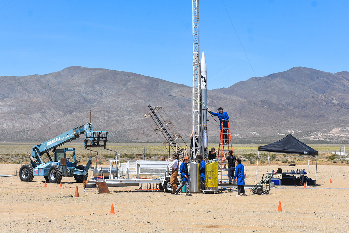 students set up a rocket for launch on the desert floor, with dry mountains in the background