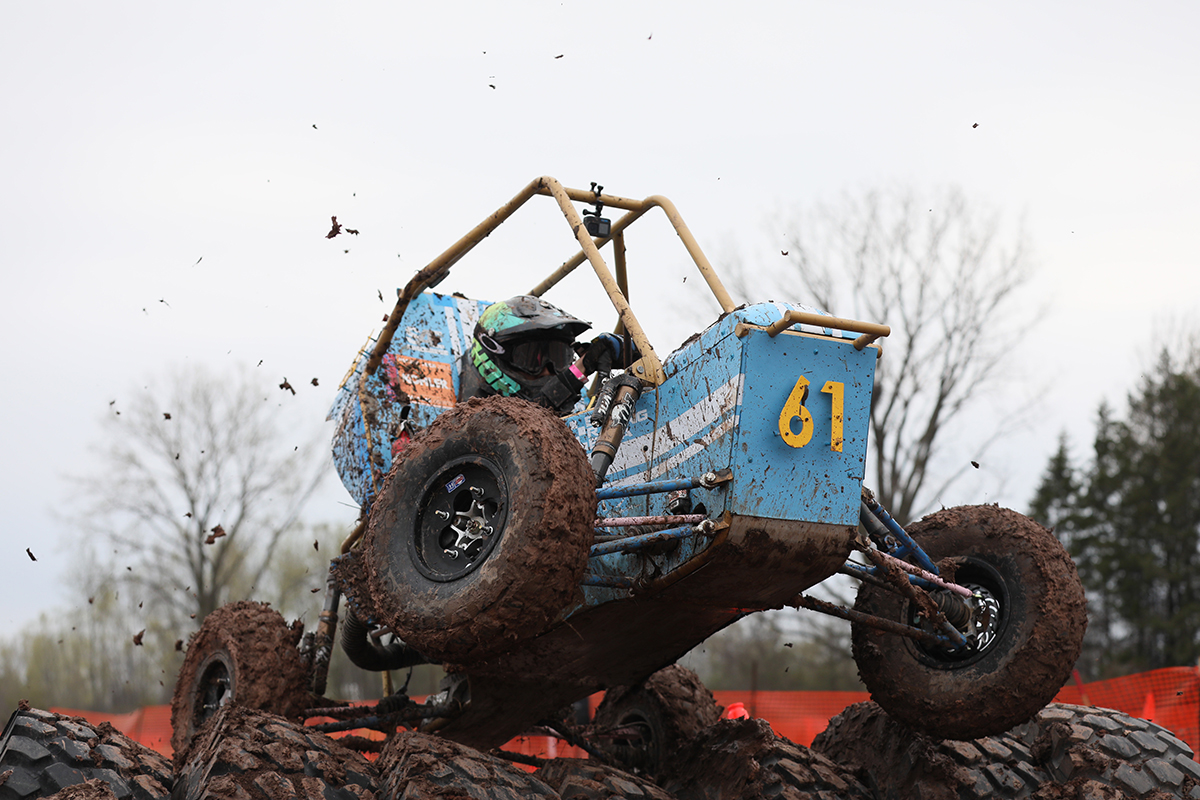 An off-road racing vehicle being driven over a muddy hill, with mud flying