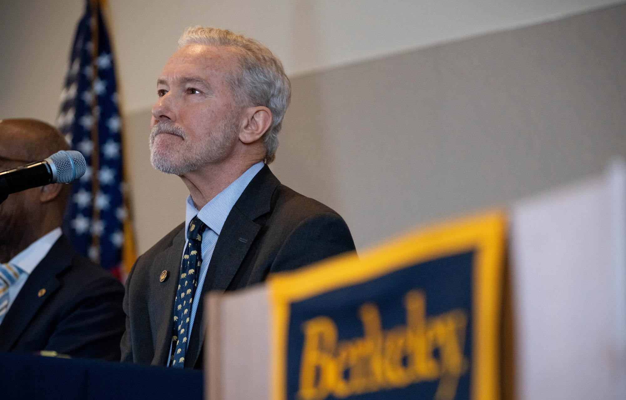 Lyons, standing next to a podium, with President Michael Drake semi-visible to his right, being announced as chancellor