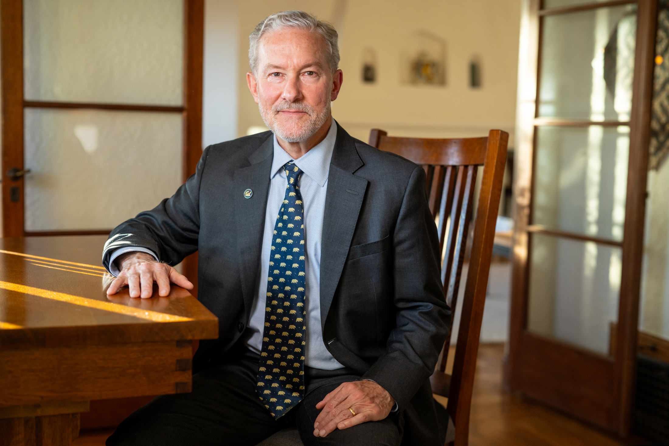 Rich Lyons, seated in a chair, at a table, wearing a suit and Berkeley bears tie