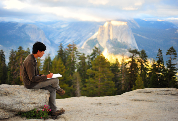 A person sits writing in a dramatic Yosemite landscape