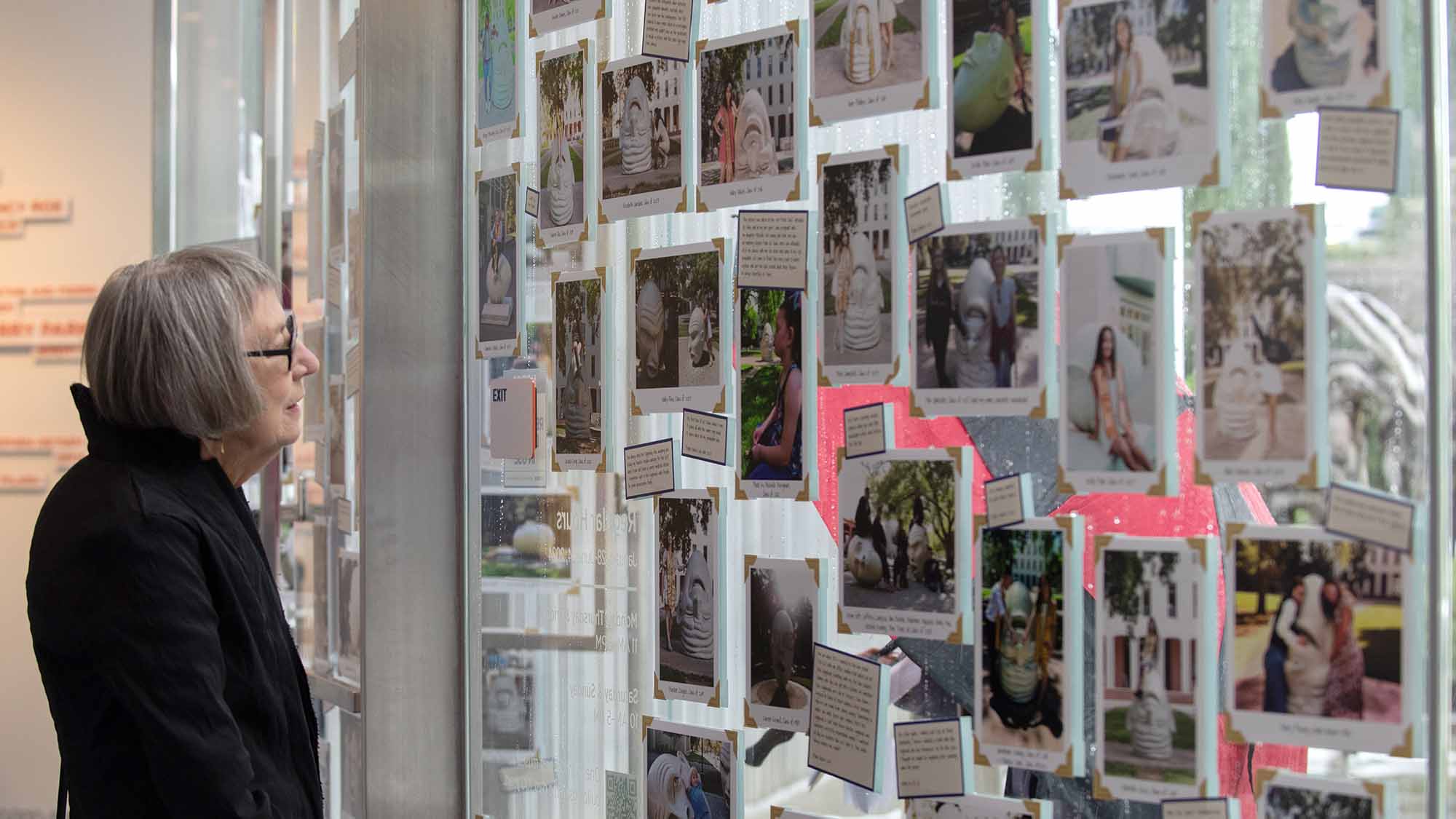 An older woman with a bob looks at photos displayed on a wall