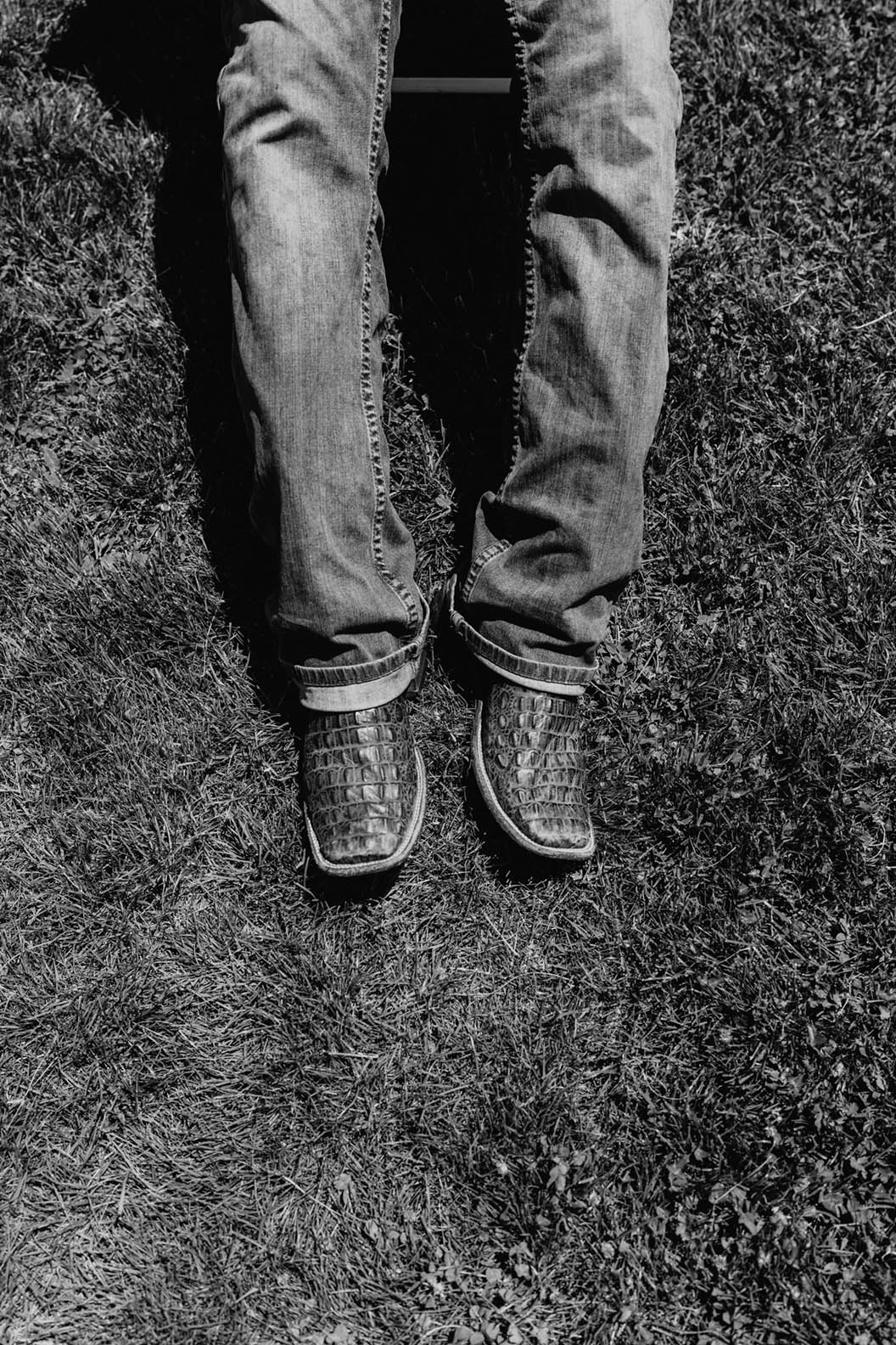 Black and white image of legs wearing jeans and cowboy boots against grass/dirt