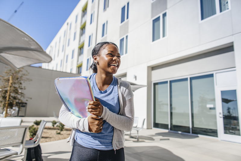 UC Merced student holds her laptop and smiles, standing in a sunny courtyard