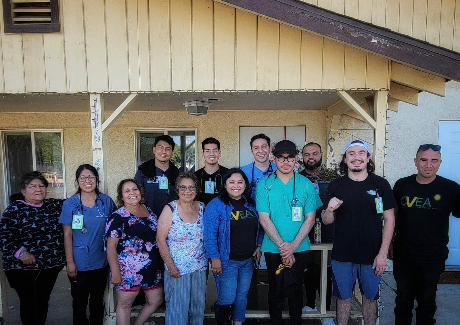 A group of people smiles for the camera in front of a yellow house