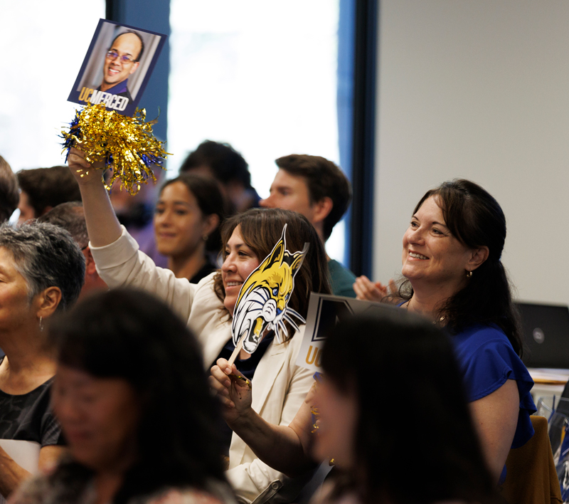 People in an audience holding UC Merced signs