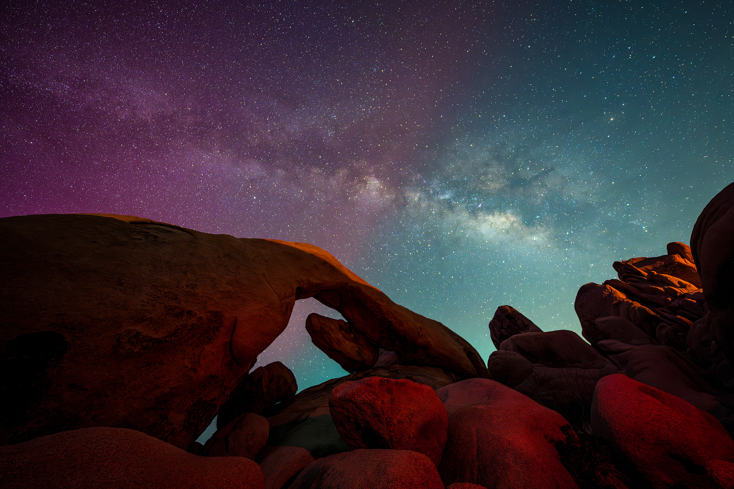Aurora borealis, in shades of magenta to pink, to teal, over a rock formation in Joshua Tree National Park.  Photo by Erik Jepsen